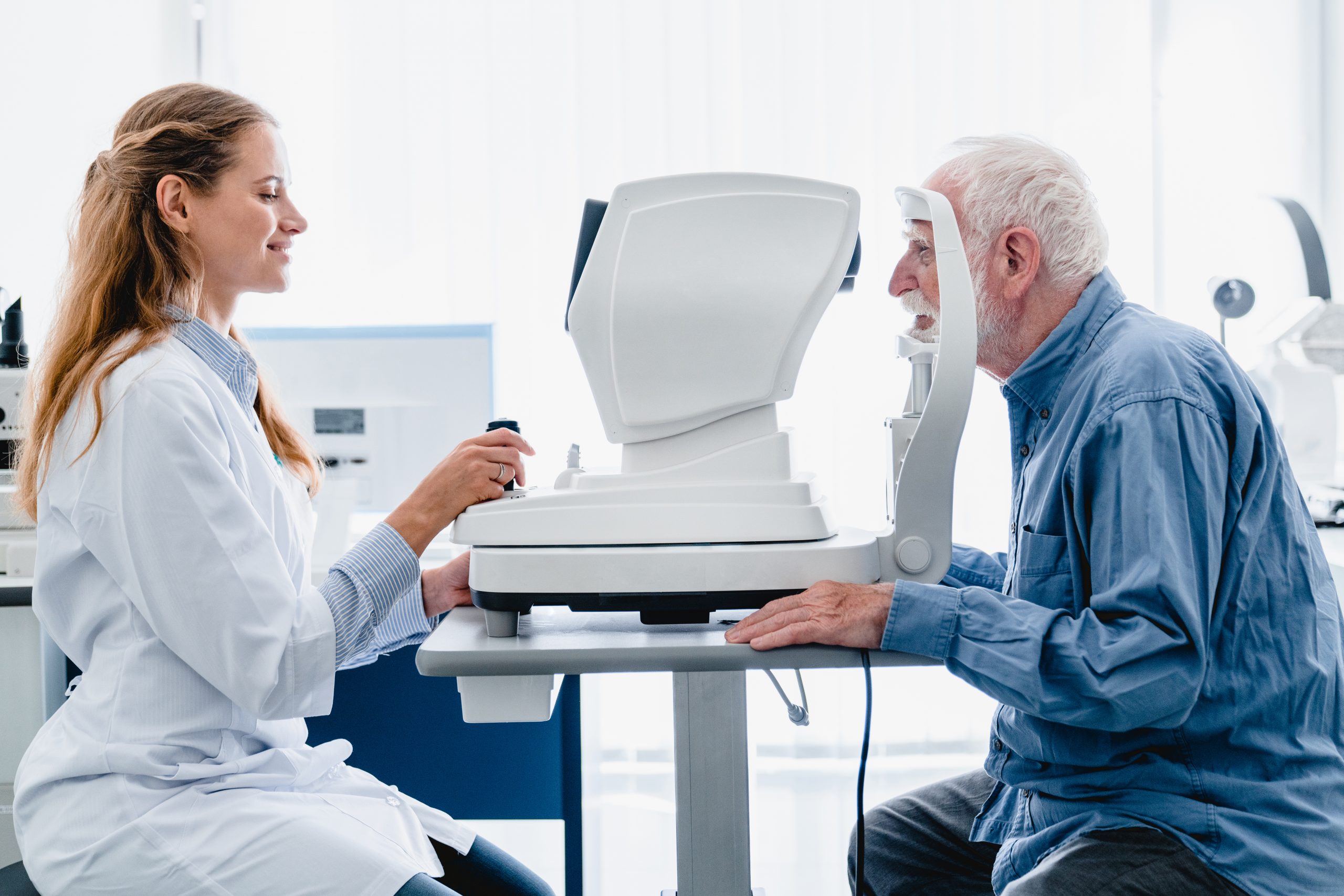 mujer joven con bata blanca de óptico - optometrista examinando la visión de un anciano